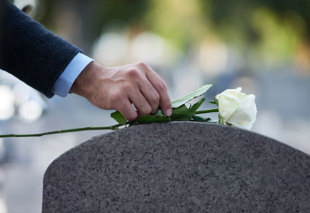 Trauernder legt weiße Rose auf einen Grabstein – stiller Abschiedsmoment auf dem Friedhof, begleitet von Bestatter Bottrop
